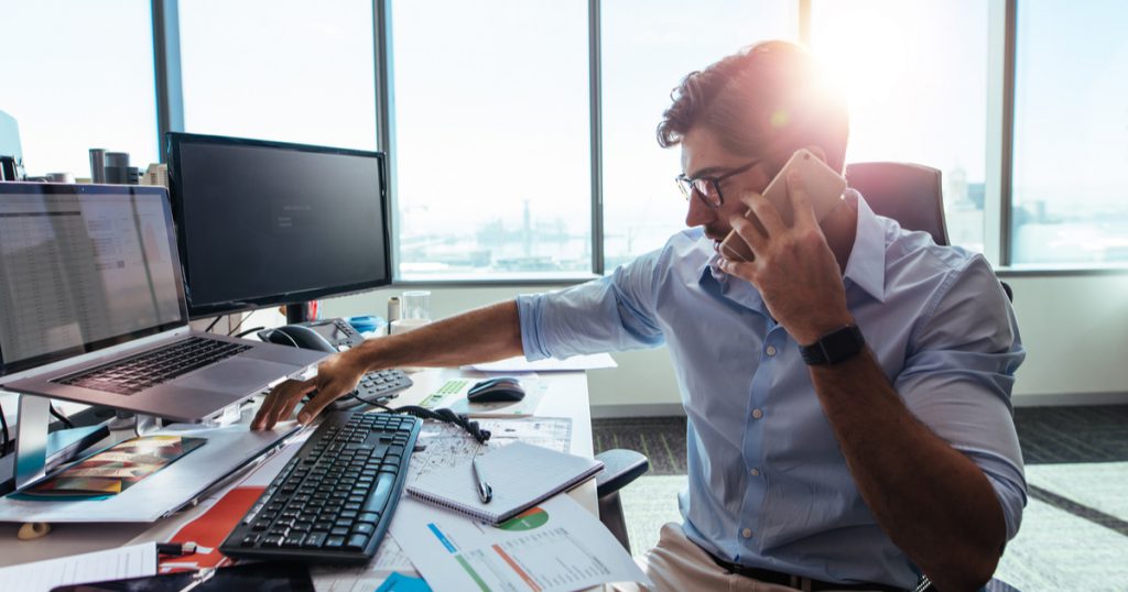 Freight broker on phone at desk using TruckLogics Trucking management system.